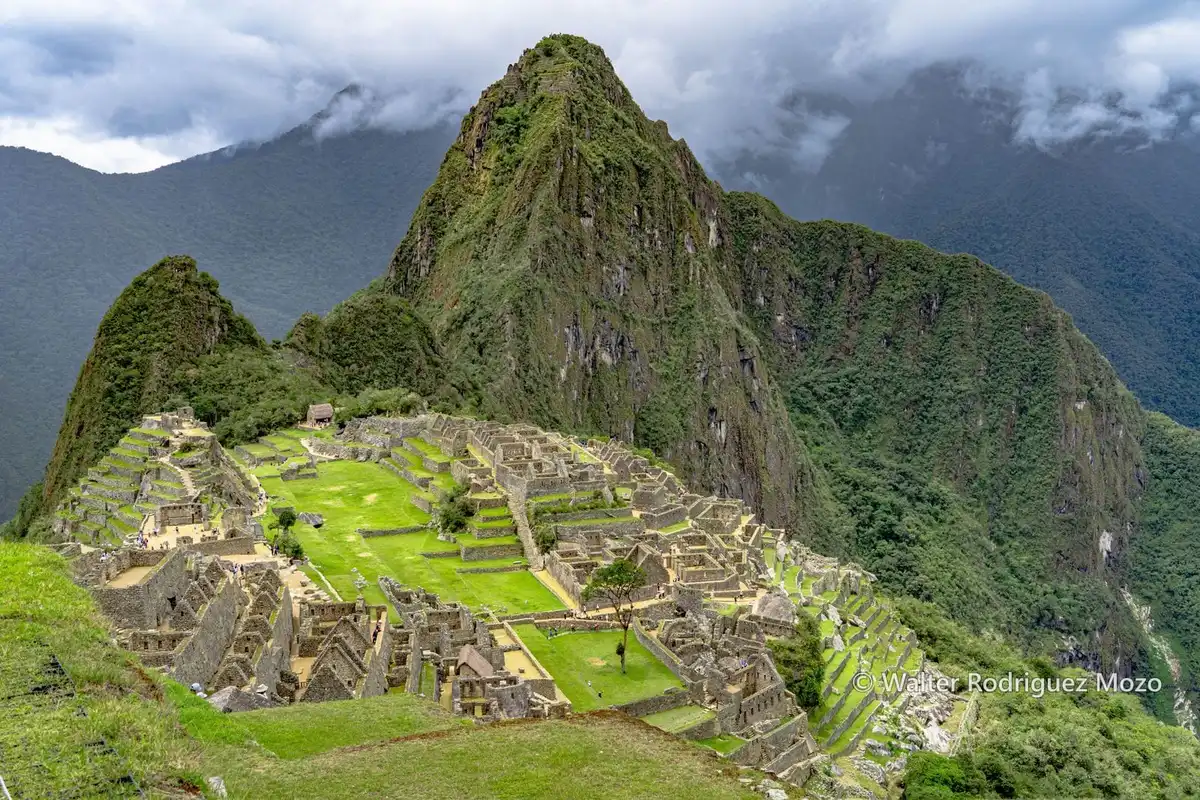 Machu Picchu citadel and its terraces with Huayna Picchu rising behind under a cloudy sky